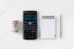 some money, a calculator, a notepad and a pen on a white background